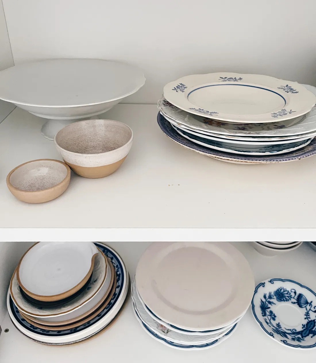 Dvě police s bílým a modrým porcelánem, miskami a talíři ve skříňce.