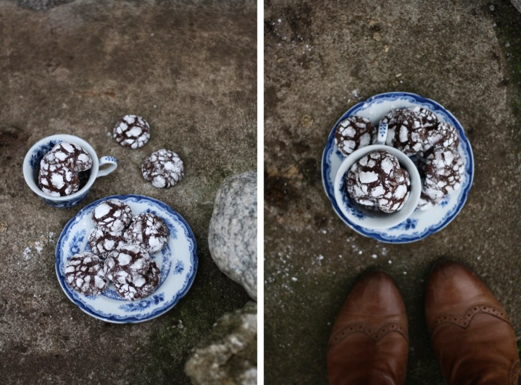 Čokoládové zasněžené crinkle sušenky s popraskaným cukrem na modrobílém porcelánu a kamenném podkladu venku.