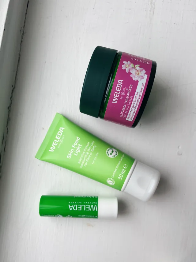 Tři produkty Weleda s divokou růží a Skin Food na bílém dřevěném parapetu.